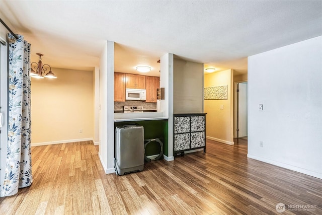 kitchen with white microwave, wood finished floors, light countertops, backsplash, and brown cabinetry