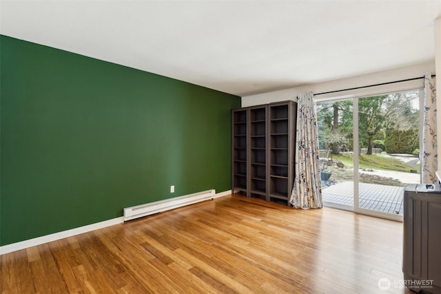 spare room featuring a baseboard heating unit, light wood-type flooring, and baseboards