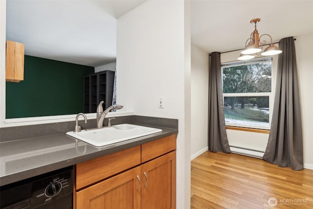 kitchen featuring dishwasher, dark countertops, hanging light fixtures, light wood-style floors, and a sink