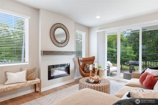 living area with light wood finished floors, a glass covered fireplace, and baseboards