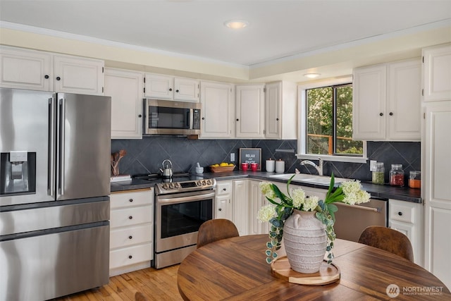 kitchen with light wood-type flooring, stainless steel appliances, white cabinets, dark countertops, and tasteful backsplash