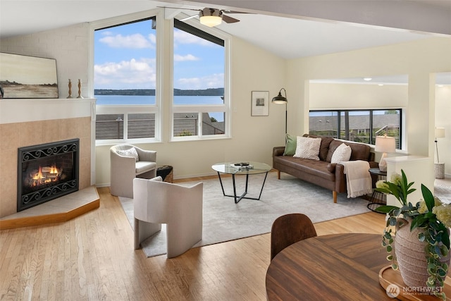 living room with lofted ceiling, wood finished floors, a water view, and a tile fireplace