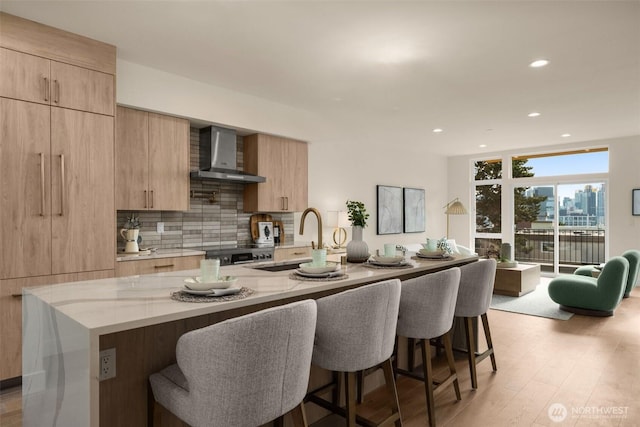 kitchen with decorative backsplash, modern cabinets, light stone countertops, wall chimney range hood, and a sink