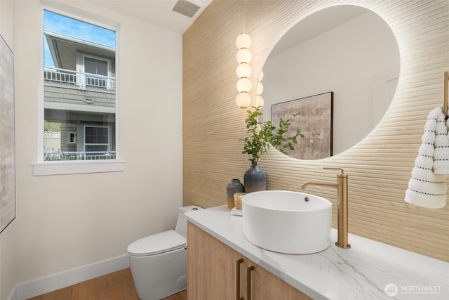 half bathroom with visible vents, plenty of natural light, vanity, and toilet