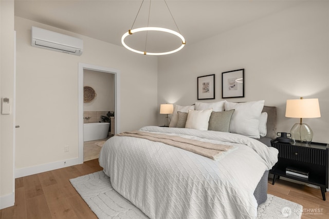 bedroom featuring ensuite bathroom, a wall mounted air conditioner, wood finished floors, and baseboards