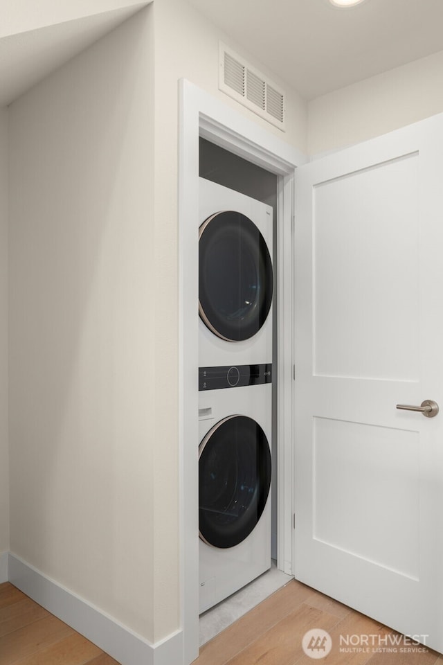 laundry room featuring laundry area, baseboards, visible vents, stacked washer / drying machine, and light wood-type flooring