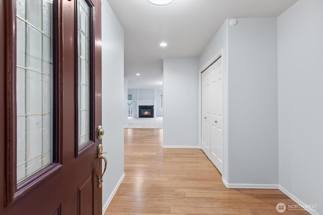 interior space with a glass covered fireplace, light wood-style flooring, recessed lighting, and baseboards