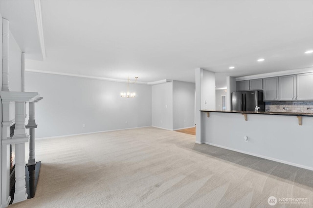 unfurnished living room featuring an inviting chandelier, recessed lighting, light colored carpet, and baseboards