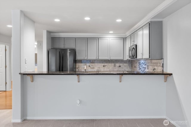 kitchen featuring dark stone countertops, gray cabinets, freestanding refrigerator, decorative backsplash, and a kitchen breakfast bar