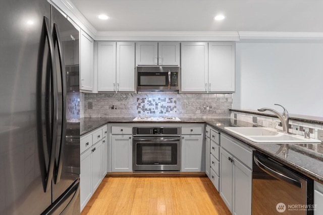 kitchen featuring light wood finished floors, dark stone counters, decorative backsplash, stainless steel appliances, and a sink