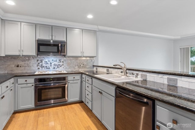 kitchen with light wood-type flooring, gray cabinets, a sink, backsplash, and appliances with stainless steel finishes