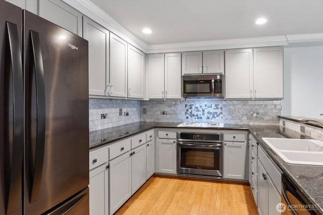 kitchen with dark stone counters, decorative backsplash, appliances with stainless steel finishes, light wood-style floors, and a sink