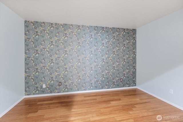 empty room with wallpapered walls, wood finished floors, and baseboards