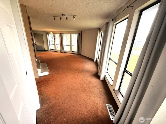 corridor featuring dark colored carpet, visible vents, a healthy amount of sunlight, and a textured ceiling