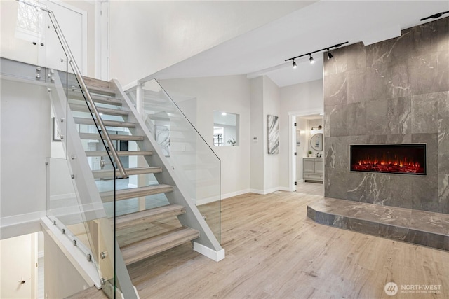 stairs featuring baseboards, a tile fireplace, wood finished floors, rail lighting, and vaulted ceiling