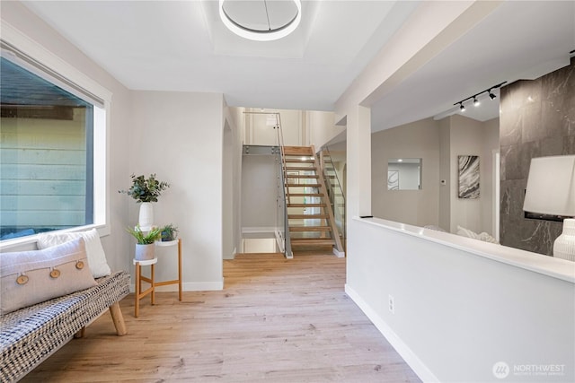 corridor with light wood finished floors, baseboards, stairway, rail lighting, and vaulted ceiling