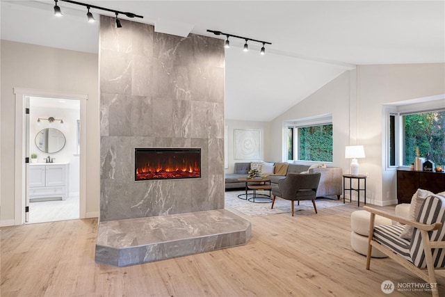 living area featuring lofted ceiling, baseboards, a tiled fireplace, and wood finished floors