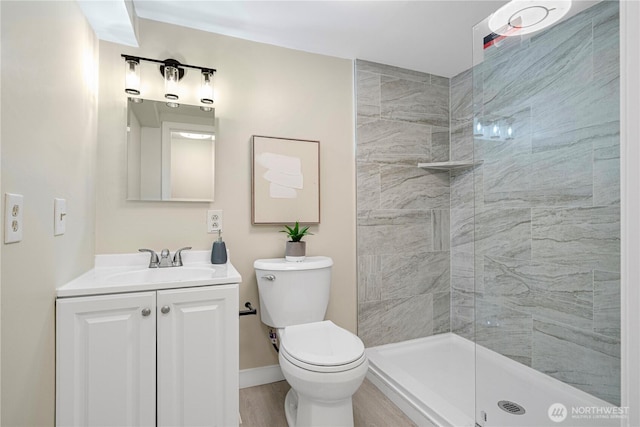 bathroom with toilet, wood finished floors, a tile shower, and vanity