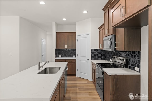 kitchen featuring a kitchen island with sink, stainless steel appliances, a sink, light wood-style floors, and light countertops