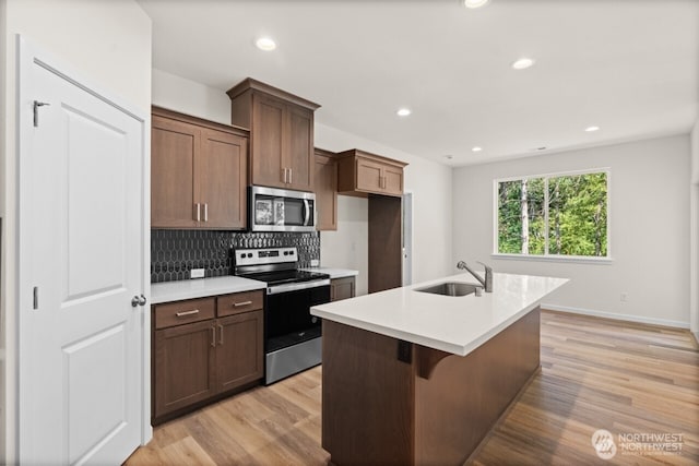 kitchen featuring stainless steel appliances, a sink, light countertops, light wood-type flooring, and backsplash