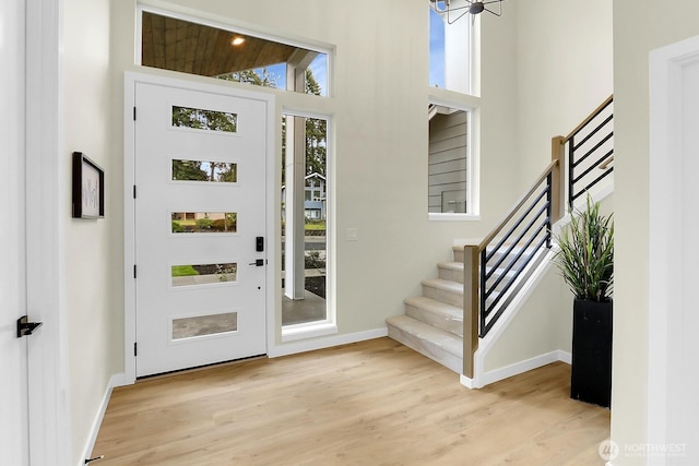 foyer with stairway, a towering ceiling, baseboards, and wood finished floors