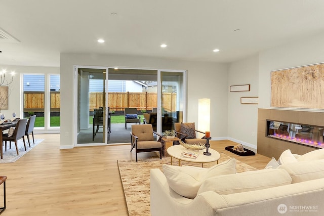 living room featuring baseboards, a tiled fireplace, light wood-style flooring, a chandelier, and recessed lighting