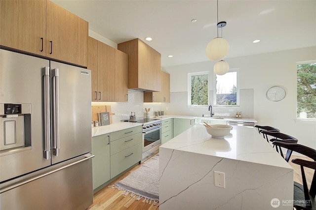 kitchen featuring pendant lighting, tasteful backsplash, a sink, light stone countertops, and high quality appliances