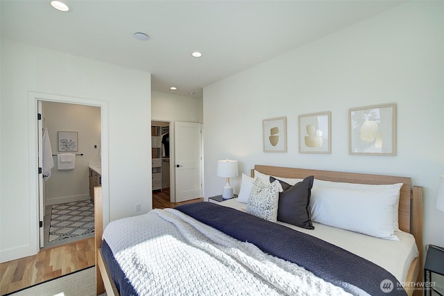 bedroom with baseboards, wood finished floors, a walk in closet, and recessed lighting