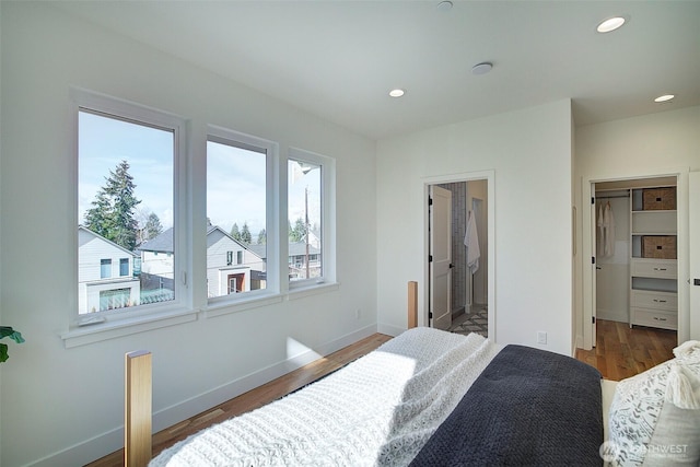 bedroom with recessed lighting, a spacious closet, ensuite bathroom, wood finished floors, and baseboards