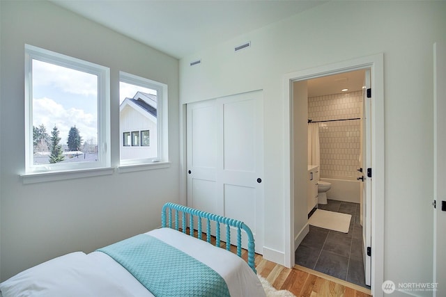 bedroom featuring a closet, visible vents, connected bathroom, and wood finished floors