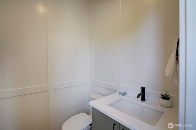 bathroom featuring a decorative wall, vanity, and toilet