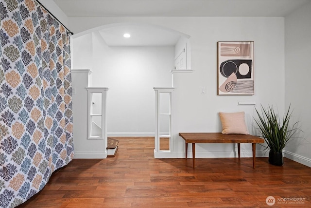 interior space with baseboards, arched walkways, and wood finished floors