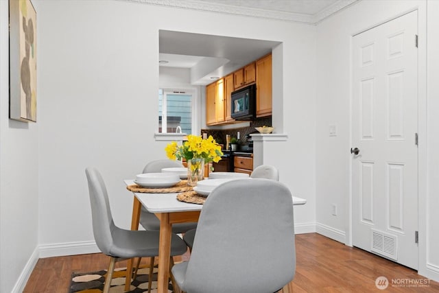 dining area featuring light wood-style flooring, baseboards, and ornamental molding