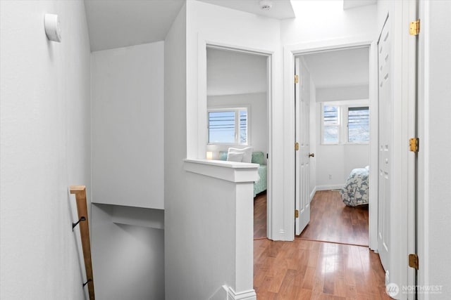 hallway featuring a wealth of natural light, baseboards, wood finished floors, and an upstairs landing