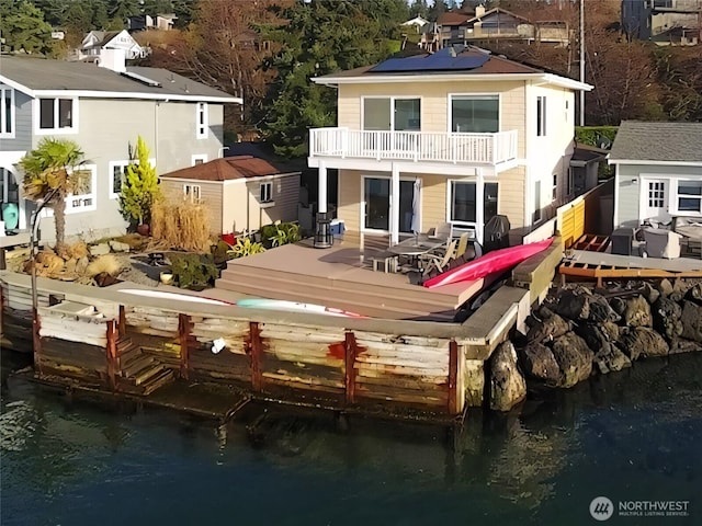 rear view of property with an outbuilding, roof mounted solar panels, a deck with water view, and a balcony