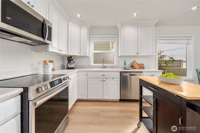 kitchen featuring light wood-type flooring, recessed lighting, white cabinets, stainless steel appliances, and a sink