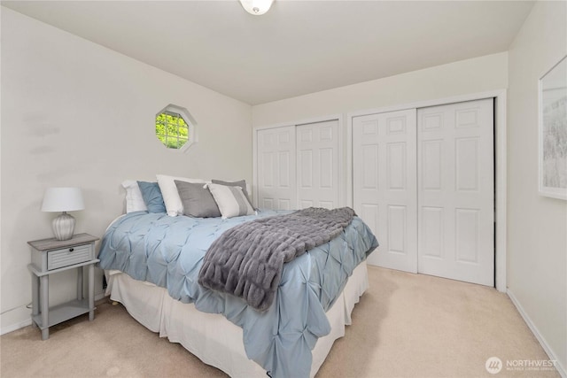 bedroom with light carpet, two closets, and baseboards