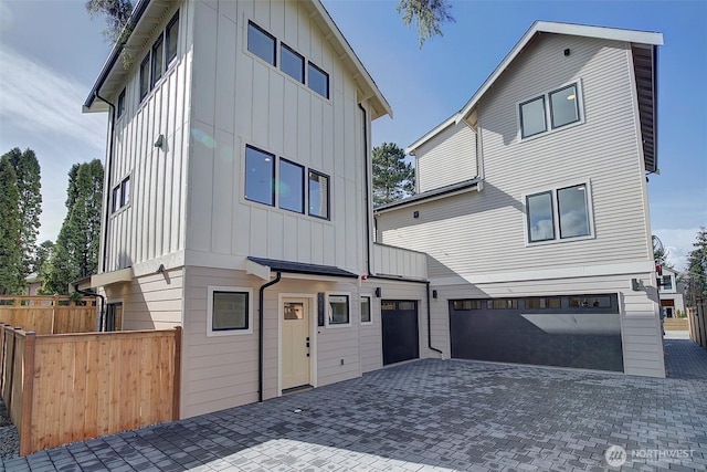 contemporary house with decorative driveway, board and batten siding, an attached garage, and fence