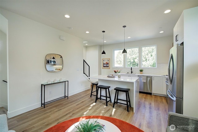 kitchen with a breakfast bar, light wood finished floors, decorative backsplash, appliances with stainless steel finishes, and white cabinetry