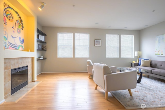 living area with baseboards, a healthy amount of sunlight, light wood-style flooring, and a tiled fireplace