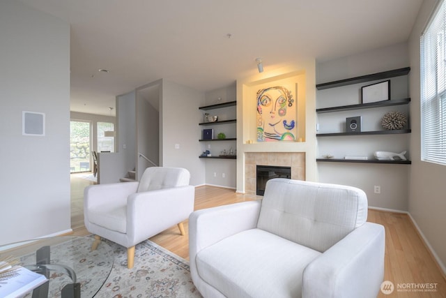 living room with baseboards, a tiled fireplace, and light wood finished floors