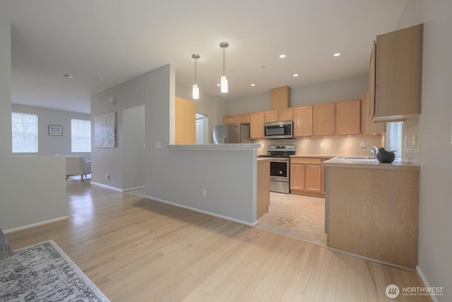 kitchen featuring stainless steel appliances, light countertops, hanging light fixtures, light brown cabinetry, and a sink