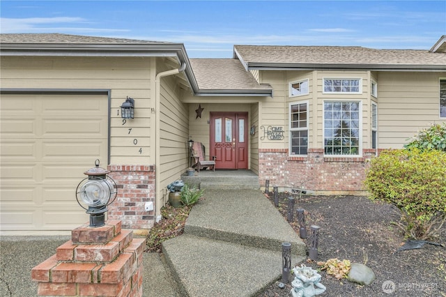 entrance to property featuring a garage, roof with shingles, and brick siding