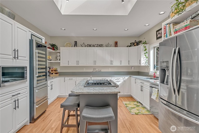 kitchen with white cabinets, light wood-style floors, a kitchen island, and stainless steel appliances