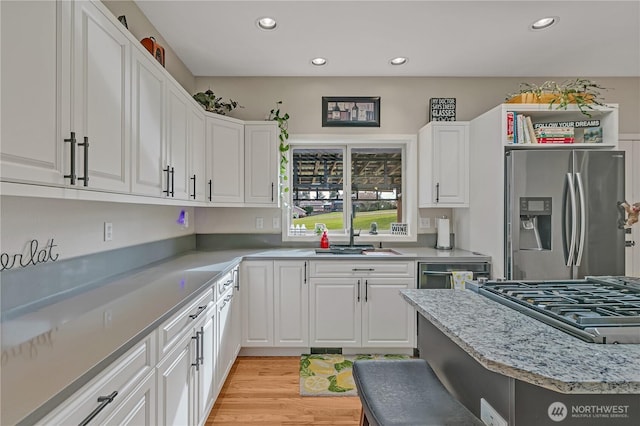 kitchen with stainless steel appliances, white cabinets, a sink, and light wood finished floors