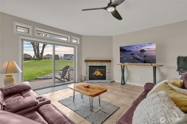 living room with baseboards, ceiling fan, a tiled fireplace, and tile patterned floors