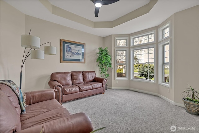 living area featuring carpet floors, a raised ceiling, a ceiling fan, and baseboards