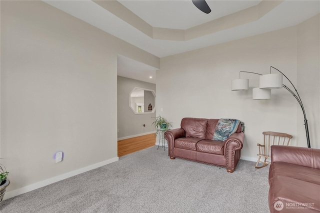 carpeted living room with ceiling fan, baseboards, and a raised ceiling