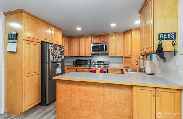 kitchen with a peninsula, a sink, light countertops, appliances with stainless steel finishes, and light wood-type flooring