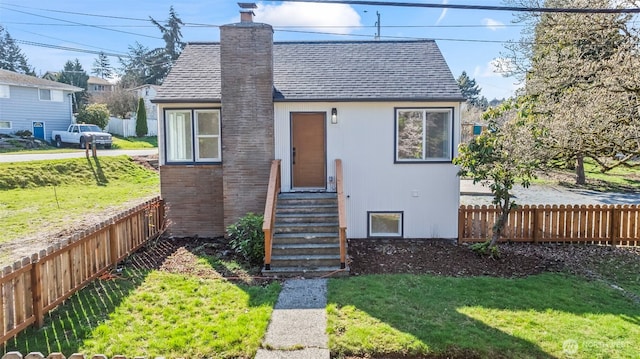 view of front of house with entry steps, a chimney, fence, and a front yard